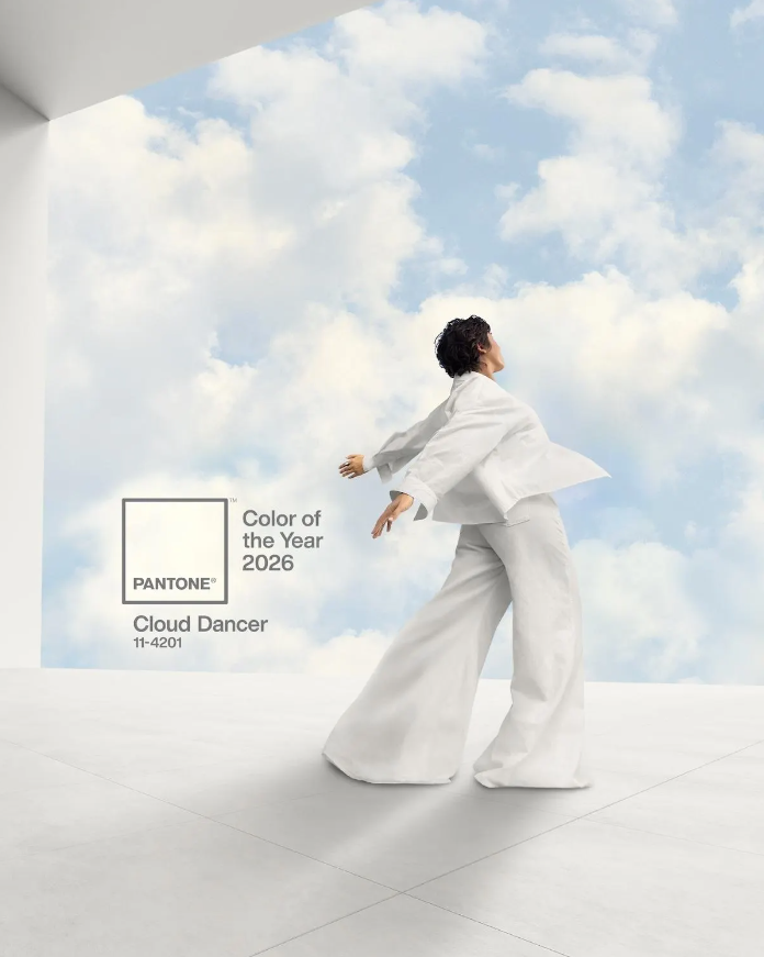 Person in a white outfit standing against a cloud-themed background with Pantone Color of the Year 2026 text.